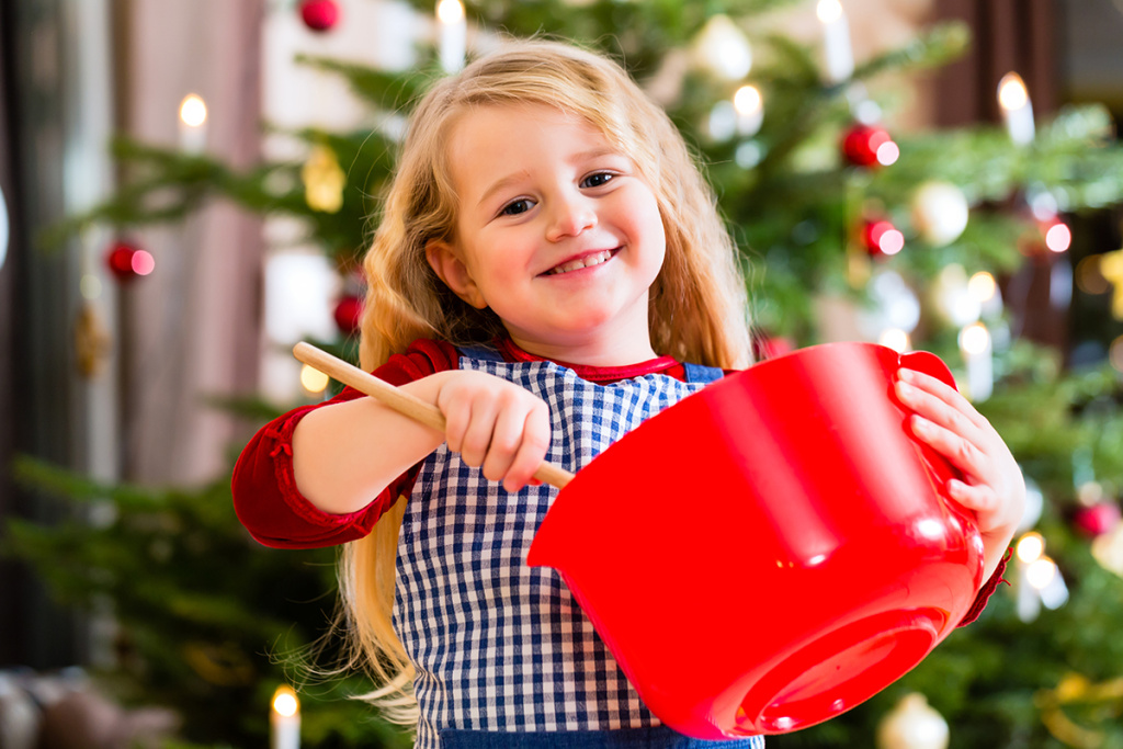 Child baking X-mas cookies at home in domestic kitchen with Christmas tree